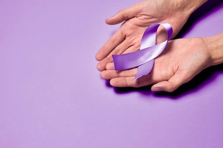 Mãos segurando laço roxo de conscientização sobre Hanseníase, representando a importância da prevenção, diagnóstico precoce e tratamento da doença.