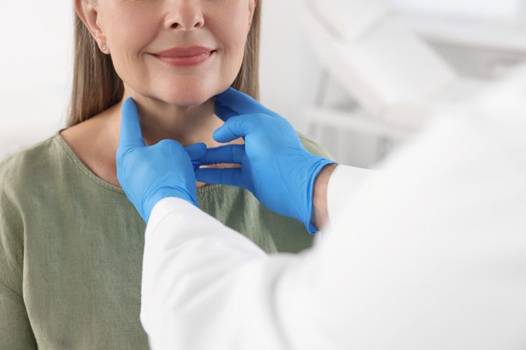 Médico realizando exame na região do pescoço de paciente, ilustrando a avaliação da Tireoide e o diagnóstico de alterações hormonais.