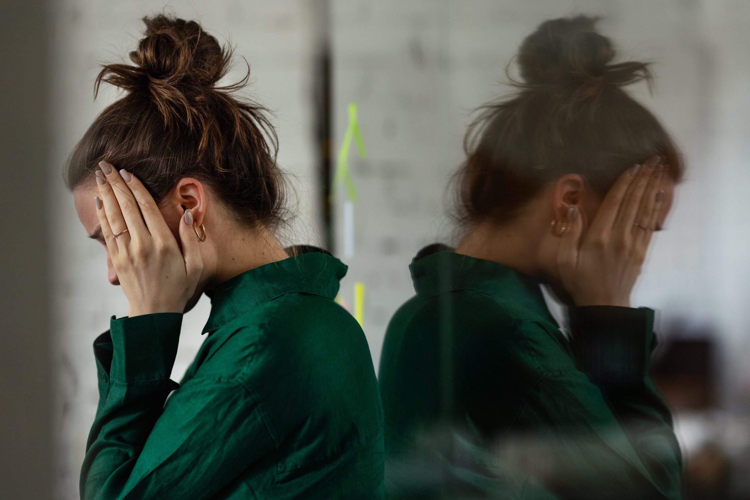 Mulher com as mãos no rosto e expressão de exaustão emocional, refletida em uma superfície espelhada, representando os impactos do burnout na saúde mental, no estresse crônico e no esgotamento relacionado ao trabalho.