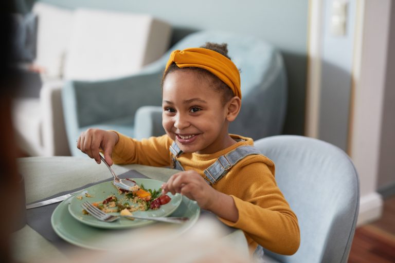 Criança sorrindo durante uma refeição com alimentos variados e nutritivos, representando a importância da alimentação saudável e equilibrada no controle e prevenção de complicações relacionadas ao diabetes infantil.