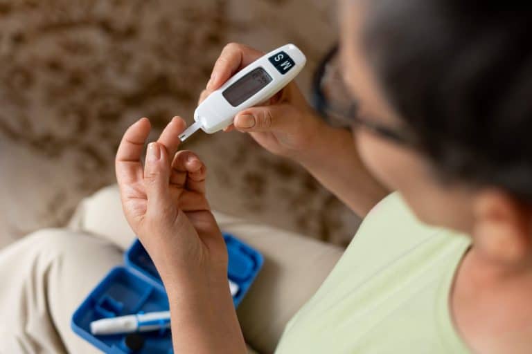 Pessoa realizando teste de glicemia com medidor digital e coleta de sangue na ponta do dedo, ilustrando os cuidados e o acompanhamento do diabetes tipo 5.