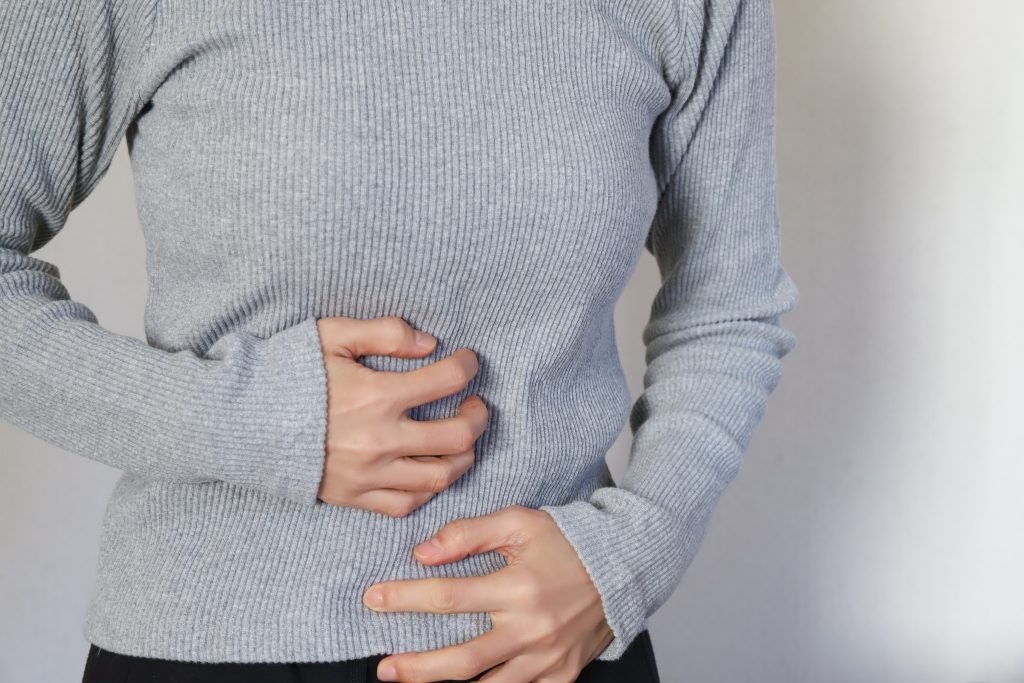 Pessoa segurando a região abdominal com expressão corporal de desconforto, ilustrando sintomas associados às doenças inflamatórias intestinais, como dor abdominal, cólicas e alterações digestivas.