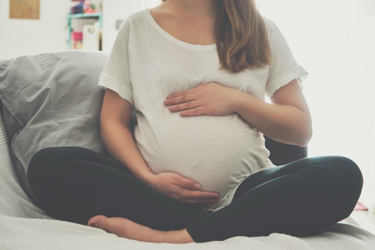 Gestante sentada com as mãos sobre a barriga durante o pré-natal, representando os cuidados na gravidez e a importância da prevenção e do acompanhamento para evitar a transmissão do HIV da mãe para o bebê.