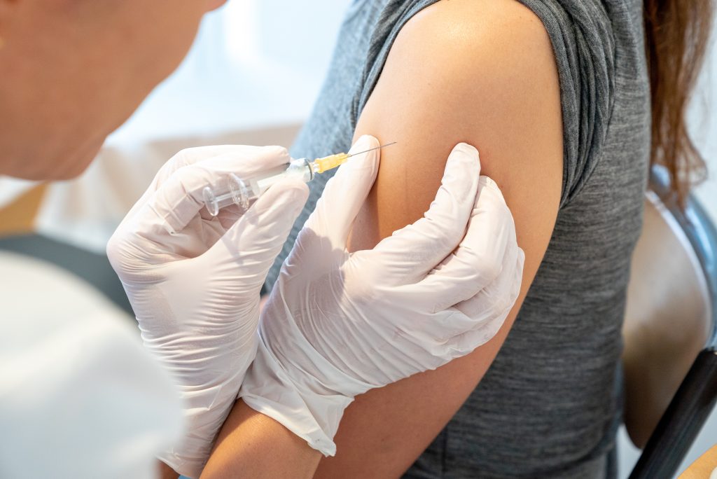 Profissional de saúde aplicando a vacina da gripe no braço de uma paciente, destacando a importância da imunização para prevenir complicações da influenza.