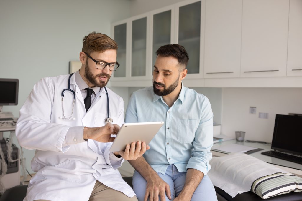 Médico orienta um paciente durante consulta, utilizando um tablet para explicar informações sobre prevenção, diagnóstico e tratamento da leishmaniose.