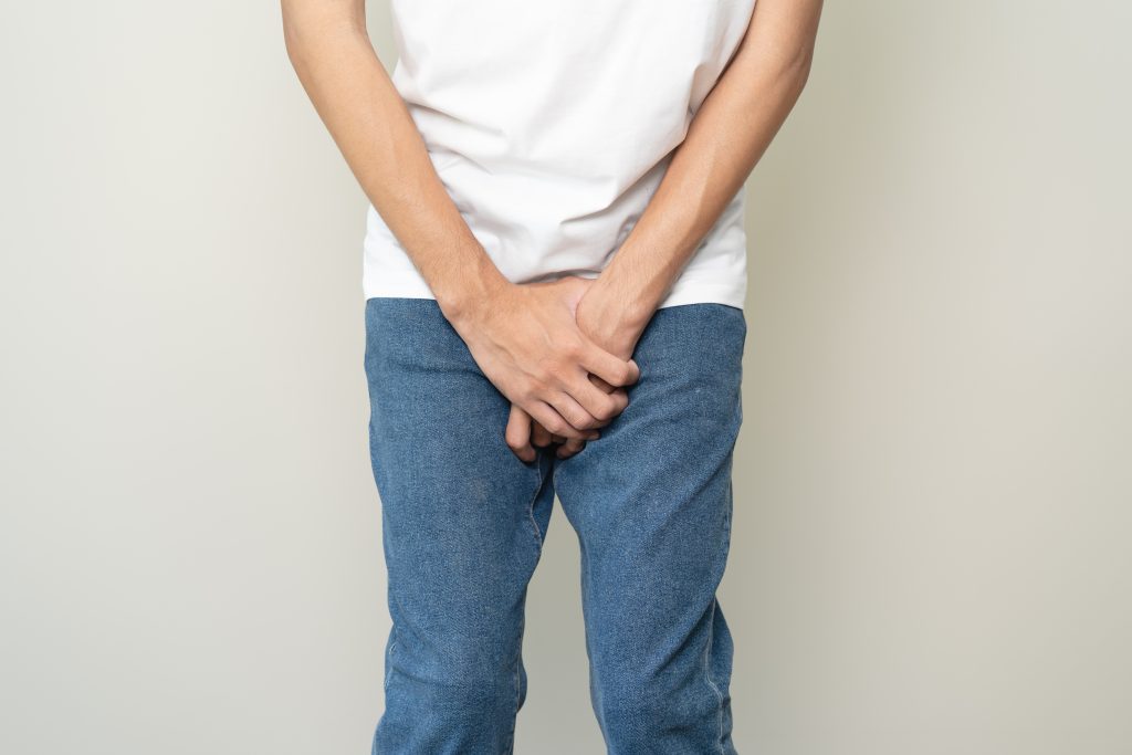 Pessoa segura a região pélvica com as mãos, ilustrando desconforto e dificuldade para urinar, um sintoma que pode indicar alterações no trato urinário e merece investigação médica.