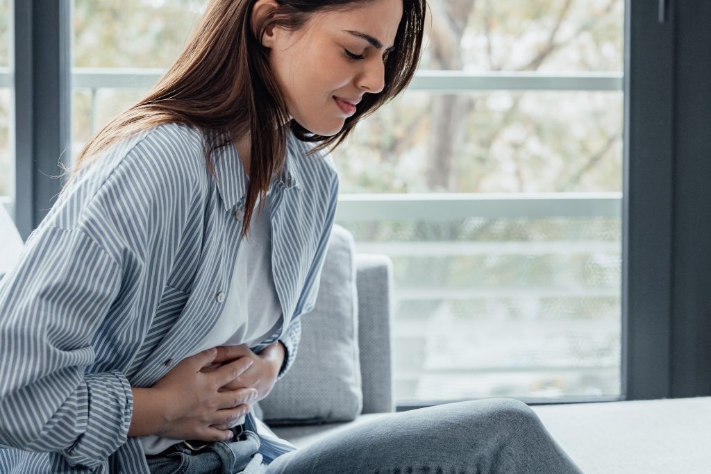 Pessoa sentada segura a região superior do abdômen com expressão de dor, ilustrando um dos principais sintomas da pancreatite, condição que exige avaliação médica e tratamento adequado.