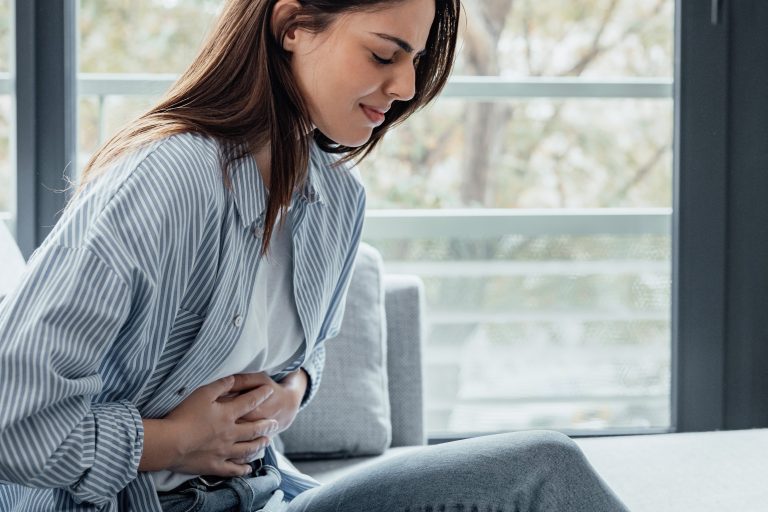 Pessoa sentada segura a região superior do abdômen com expressão de dor, ilustrando um dos principais sintomas da pancreatite, condição que exige avaliação médica e tratamento adequado.