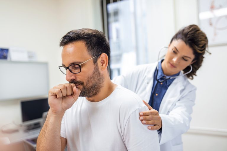 Pessoa com tosse sendo examinada por uma médica com estetoscópio, ilustrando a avaliação clínica para diagnóstico da pneumonia diante de sintomas respiratórios persistentes.