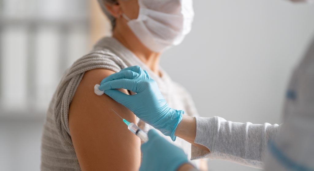 Profissional de saúde preparando a aplicação de uma vacina no braço de uma paciente, ilustrando a vacinação e os cuidados relacionados à vacina da dengue.