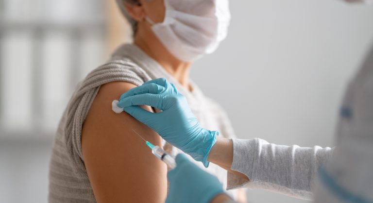 Profissional de saúde preparando a aplicação de uma vacina no braço de uma paciente, ilustrando a vacinação e os cuidados relacionados à vacina da dengue.