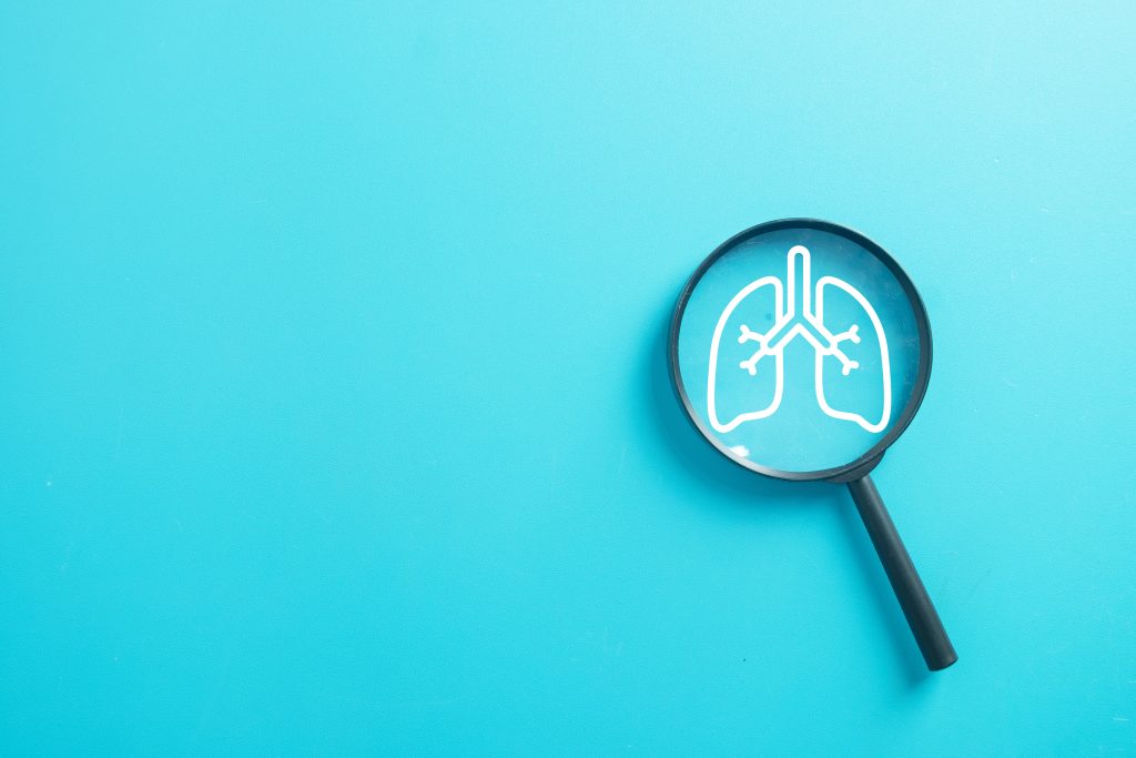 Ilustração de pulmões observados por uma lupa, representando a atenção aos sintomas, prevenção e diagnóstico do câncer de pulmão.
