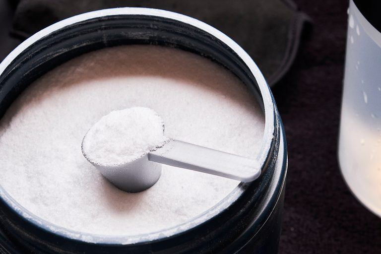 Pote de creatina em pó com dosador cheio, representando o uso de suplementos alimentares e os cuidados necessários para evitar riscos à saúde dos rins.