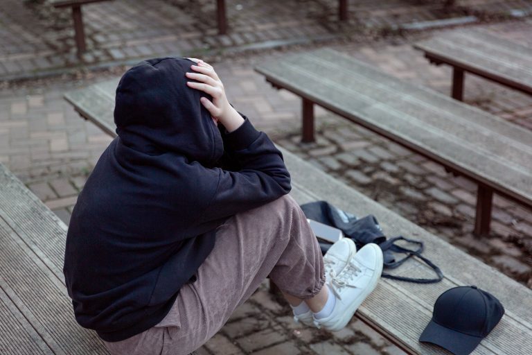 Adolescente sentado sozinho e com a cabeça baixa, representando isolamento e sofrimento emocional que podem estar relacionados à depressão na adolescência.