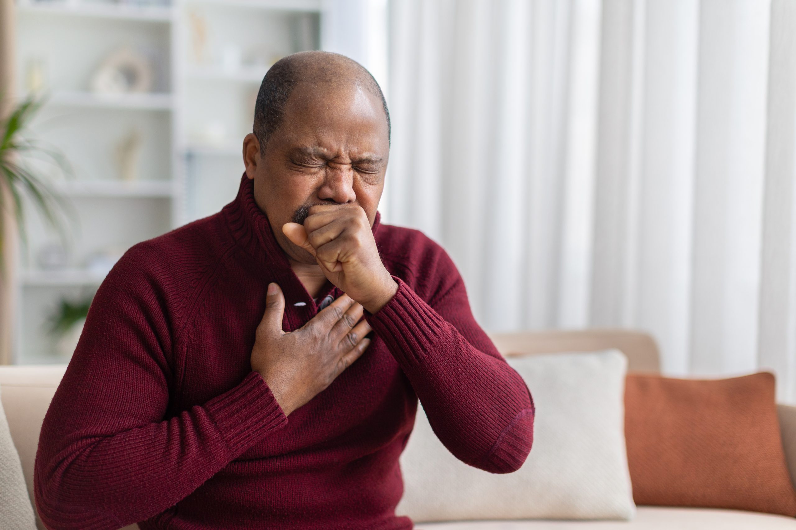 Homem tosse com a mão próxima à boca e toca o peito, representando episódio de tosse seca e irritação das vias respiratórias.