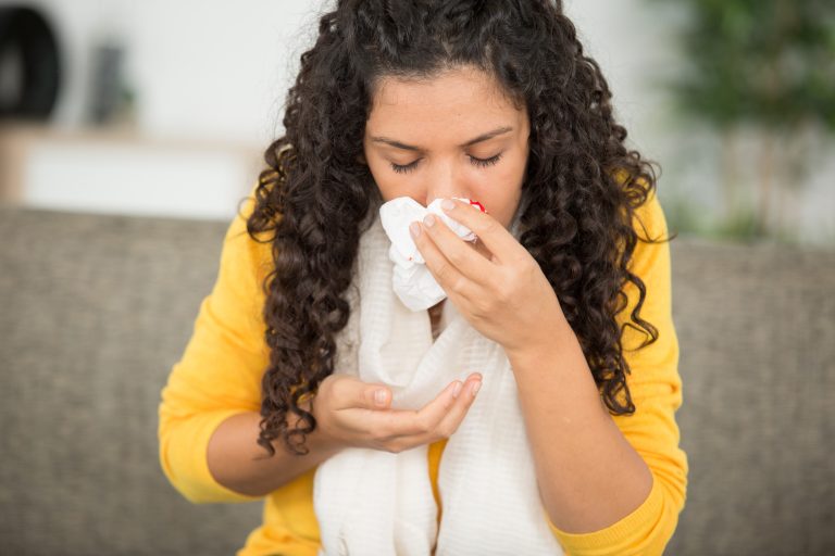 Mulher apresenta sangramento nasal e utiliza um lenço para conter o sangue, sintoma que pode levantar dúvidas sobre sua relação com a pressão alta.