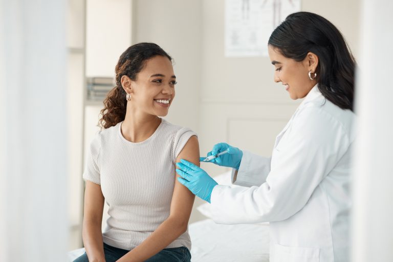 Profissional de saúde aplicando uma vacina no braço de uma mulher adulta, destacando a importância de manter a vacinação em dia para prevenir doenças.
